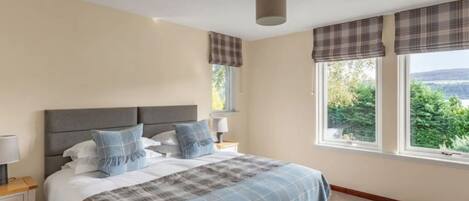 A bedroom with a bed, nightstands, a window with curtains, and a view of greenery outside.