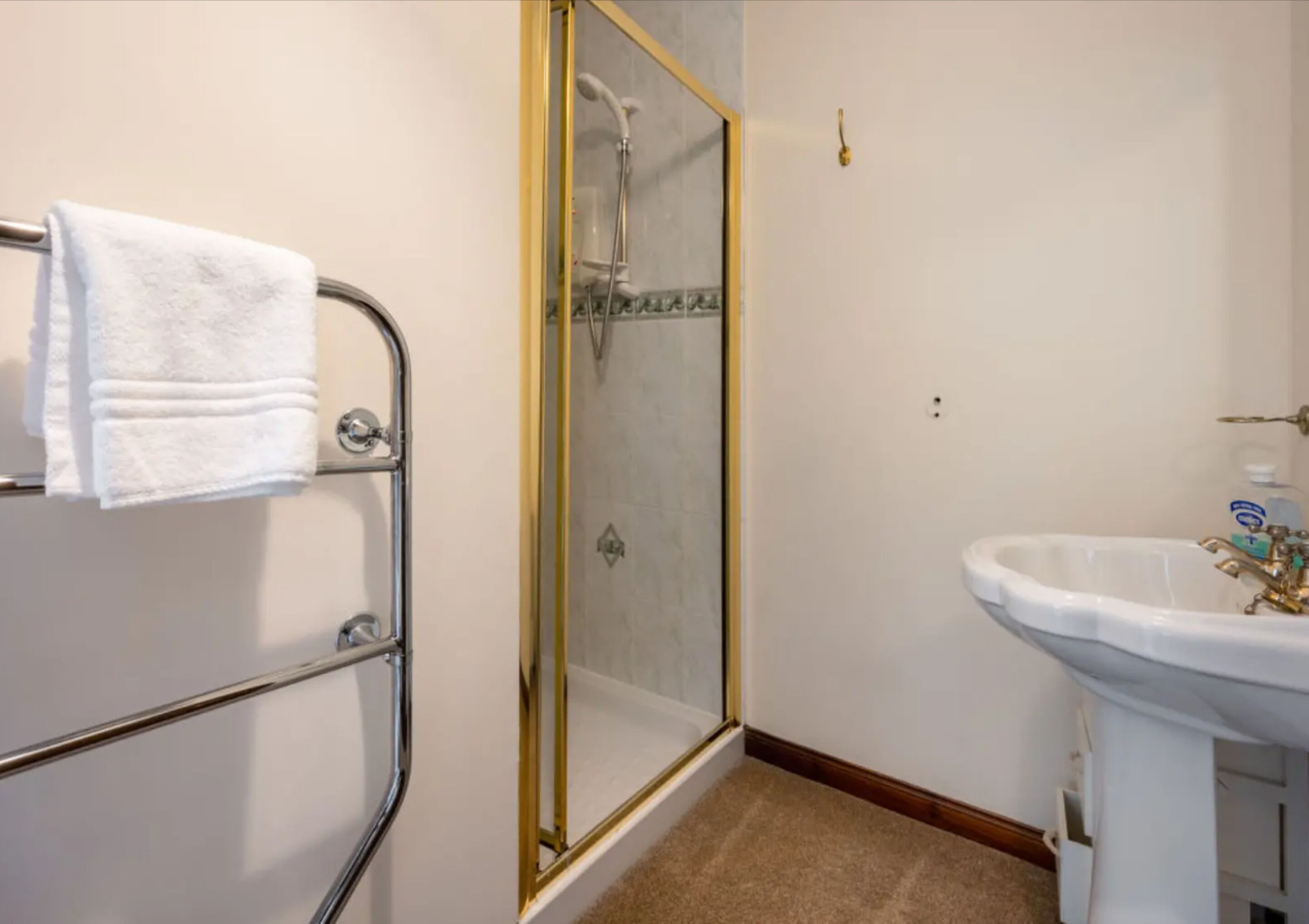 A bathroom with a glass-enclosed shower, a white sink, and a towel rack with folded towels.