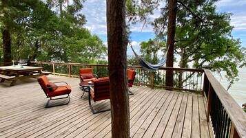 A wooden deck with outdoor furniture, including chairs and a table, overlooking a body of water.