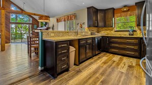 A kitchen with dark wood cabinets, a granite countertop, and a large island. - Lakefront “Treehouse”: Private Retreat in the Pines! (Point Blank)