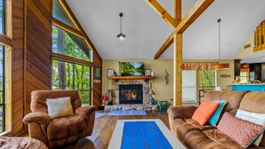 A cozy living room with a fireplace, wooden walls, and large windows. - Lakefront “Treehouse”: Private Retreat in the Pines! (Point Blank)