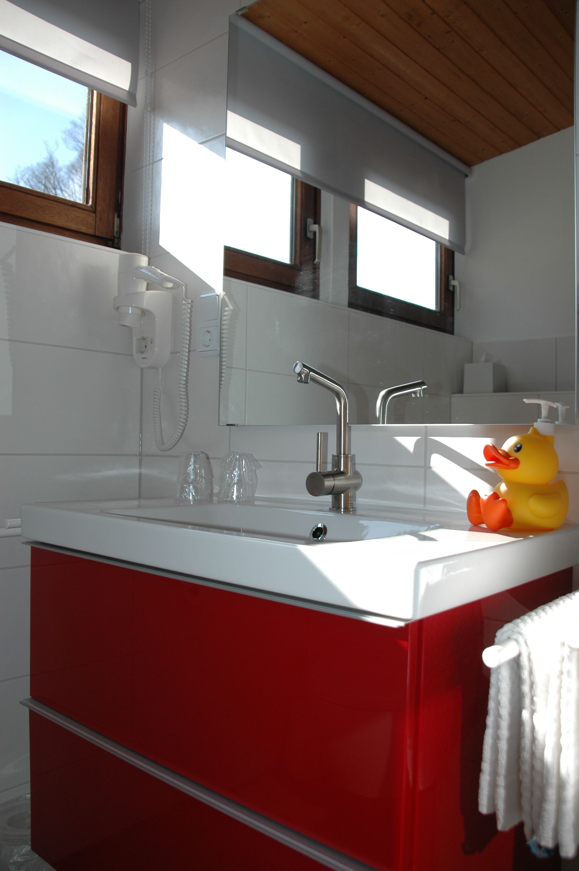 A modern bathroom with a red vanity, a white sink, and a yellow rubber duck.