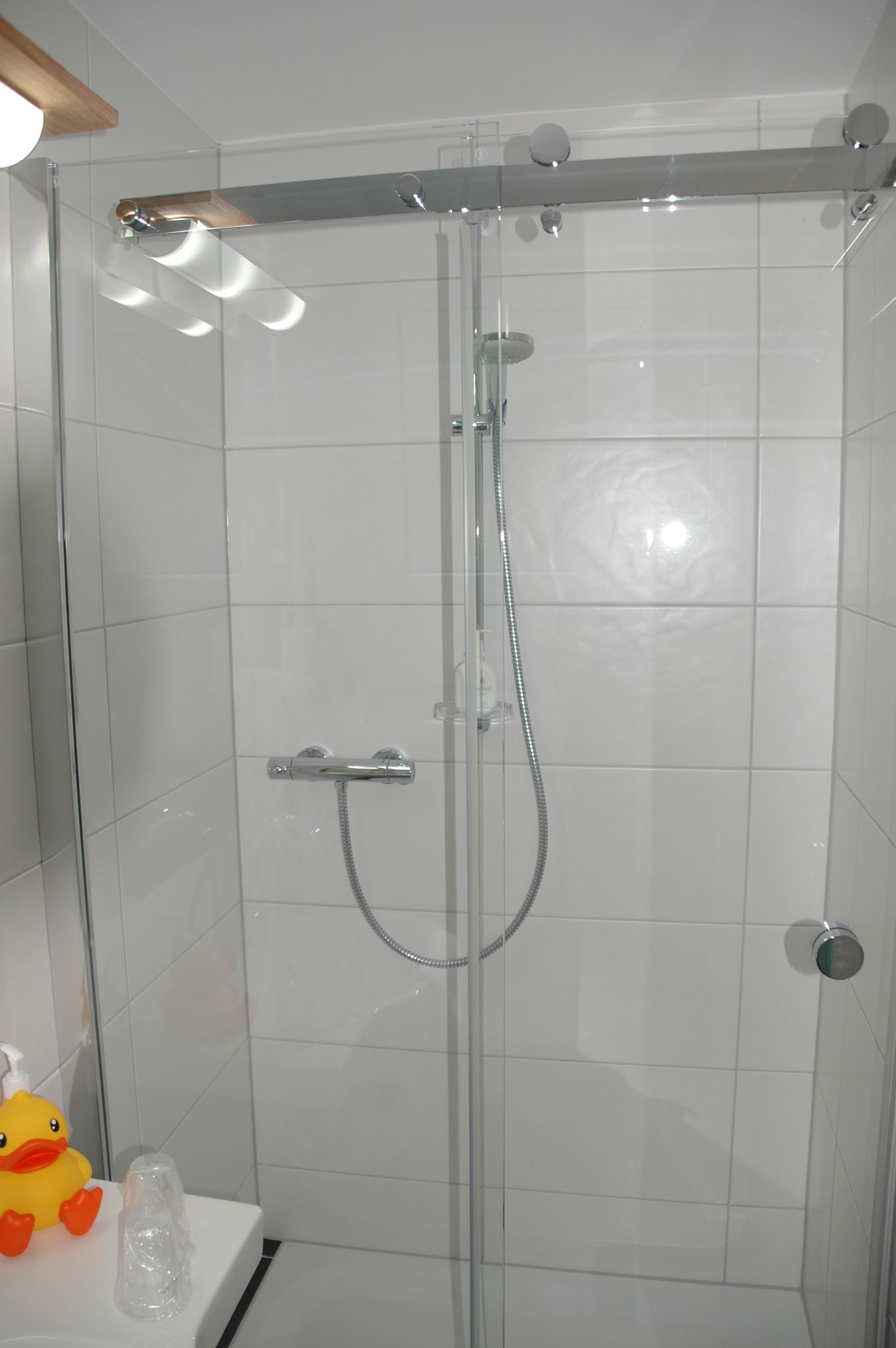 Een douchecabine met glazen wanden, een handdouche en een wandmengkraan.