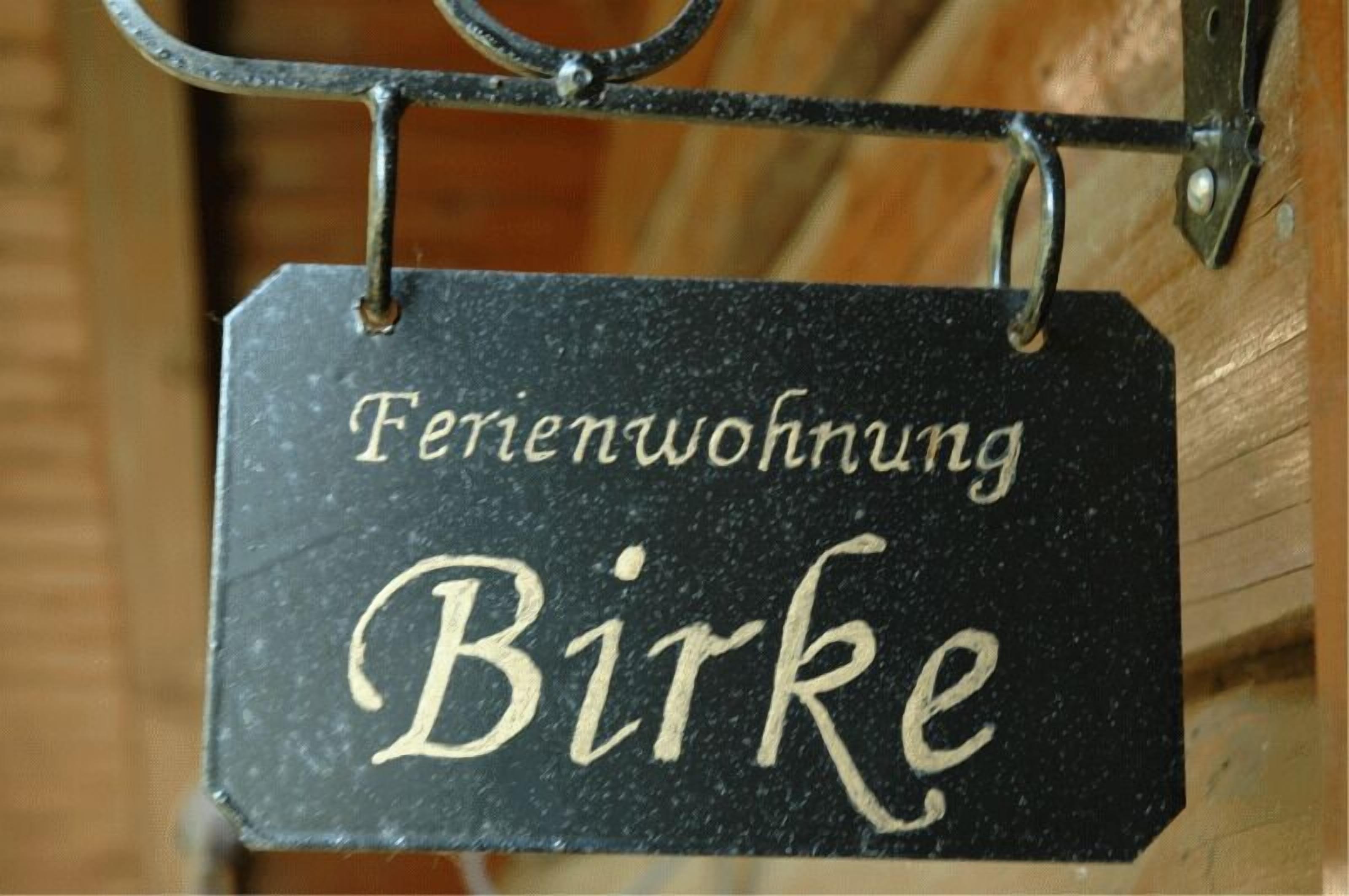 Een zwart bord met de tekst 'Ferienwohnung Birke' in wit, dat een vakantiewoning genaamd Birke aangeeft.