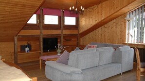 A wooden cabin interior with a sofa, a television, and a window with a view. - Pension Haus Diefenbach (Heimbach)