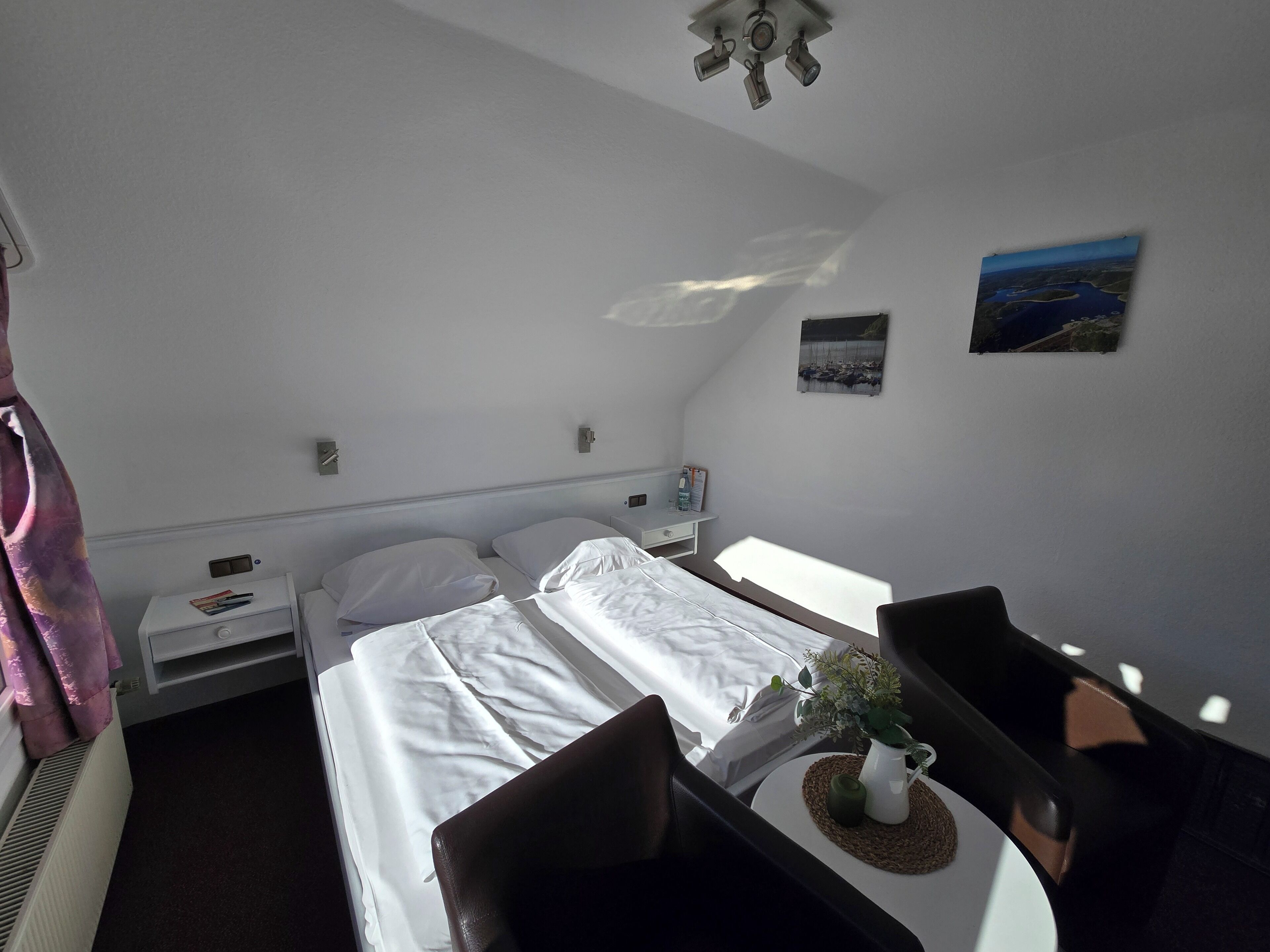 Habitació d'hotel amb dos llits, una taula petita amb una planta, una tauleta de nit i un quadre penjat a la paret.