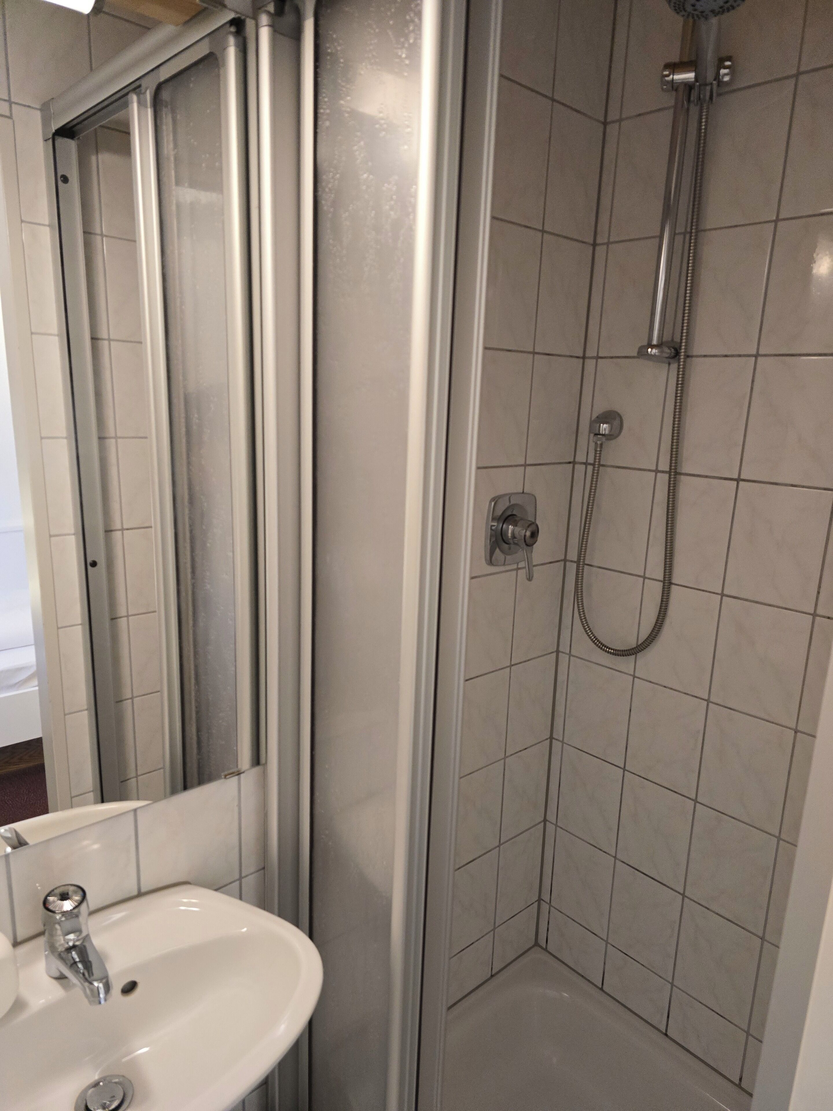 A bathroom with a glass-enclosed shower, a white sink, and a mirror.