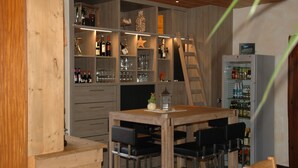 A wooden interior with a dining table, chairs, shelves with bottles and glasses, and a refrigerator. - Pension Haus Diefenbach (Heimbach)