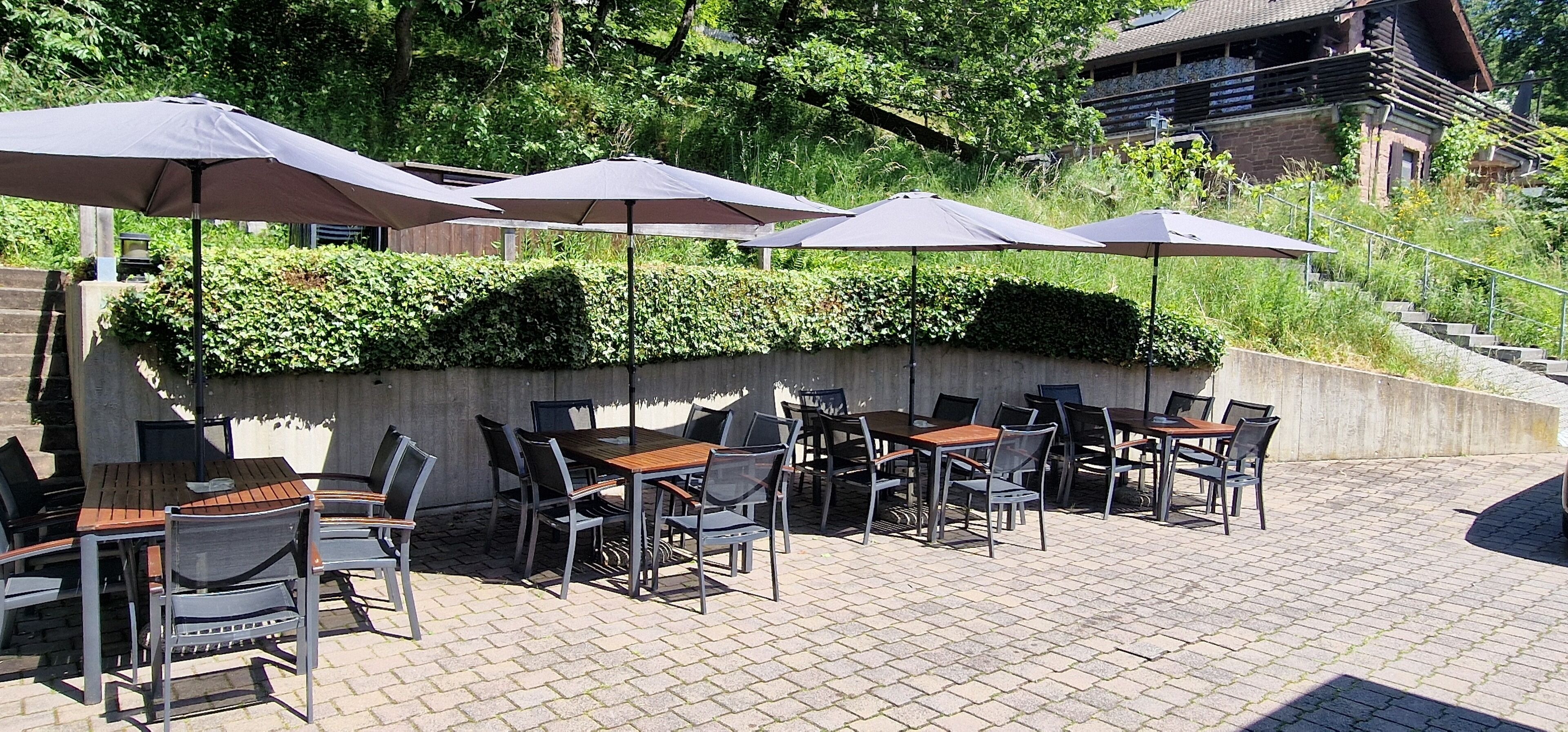 Un patio al aire libre con mesas y sillas, sombrillas y un muro de concreto con plantas.