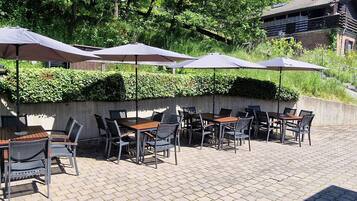 Un patio al aire libre con mesas y sillas, sombrillas y un muro de concreto con plantas.