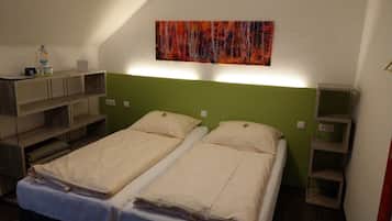 A room with two beds, a green headboard, a shelf with a bottle, and a painting on the wall.