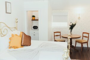 A bedroom with a bed, bedside table, and a small dining area with chairs and a table.