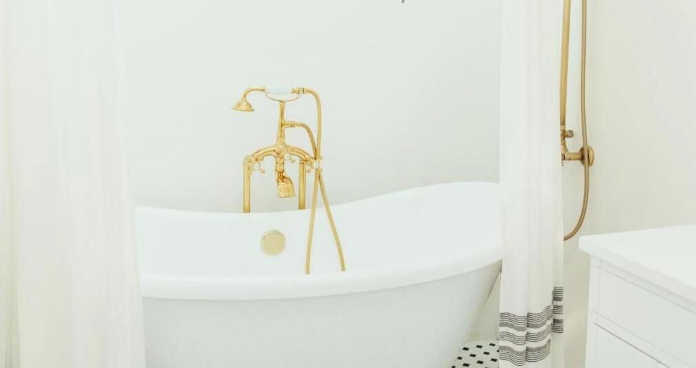 A white bathtub with a gold faucet and showerhead, a white shower curtain, and a white sink with a white countertop.