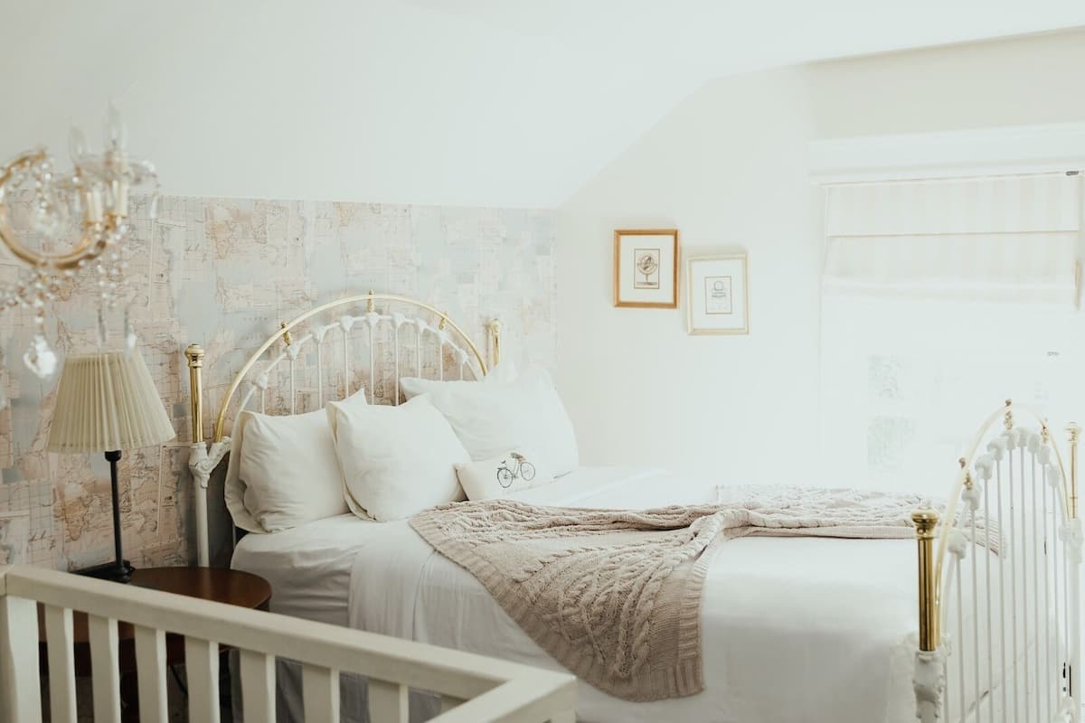 Une chambre avec un lit blanc, un papier peint représentant une carte, un lustre et un tableau encadré accroché au mur.