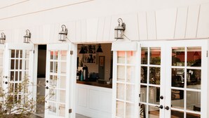 A building with white doors and windows, a wooden deck, and a planter with green foliage. - La Villa de Adelina (Ensenada)