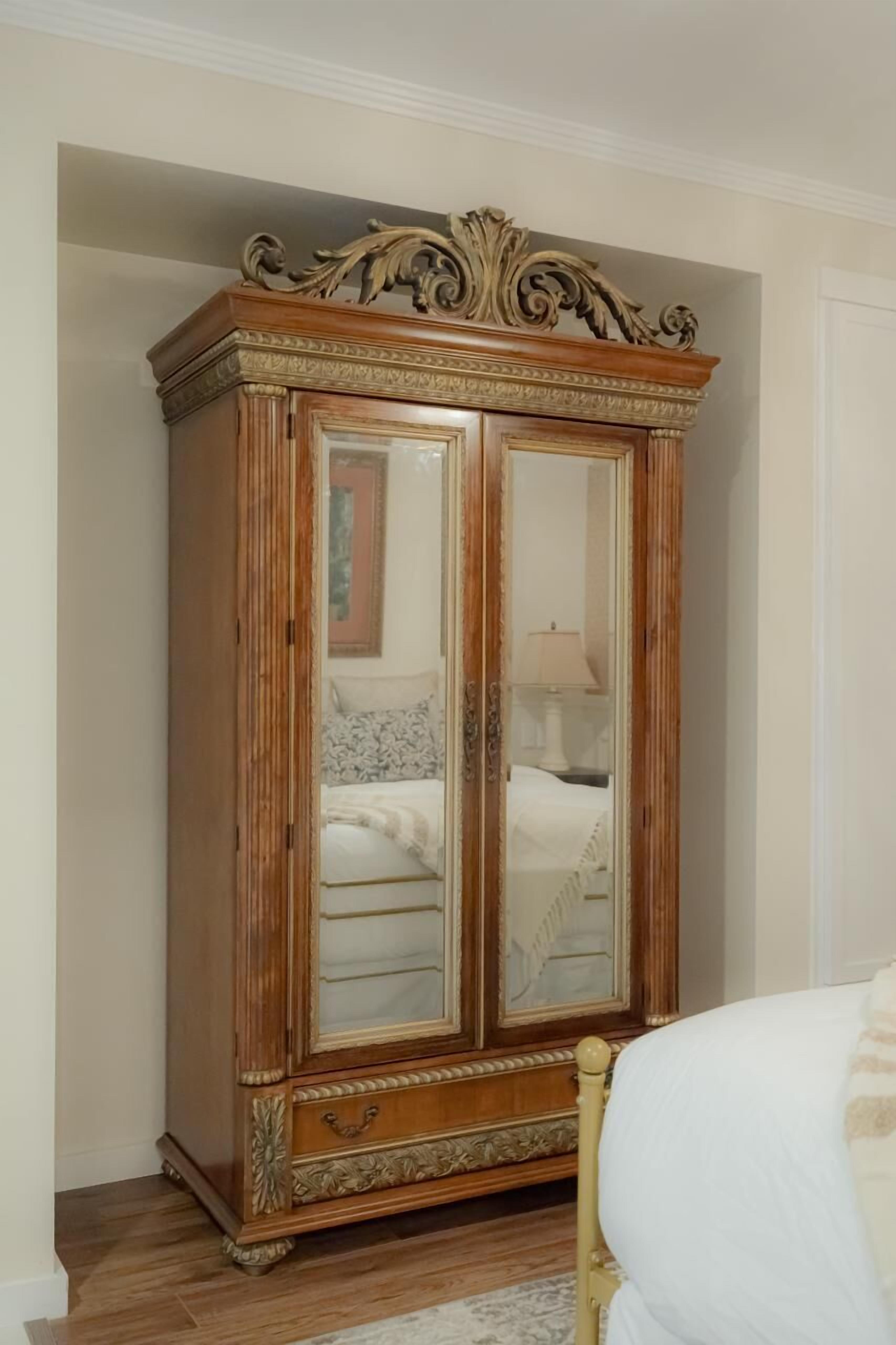 A wooden armoire with glass doors, positioned against a wall in a room with a bed and a nightstand.