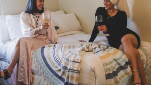 Two people sitting on a bed with a patterned blanket, holding glasses of wine. - La Villa de Adelina (Ensenada)