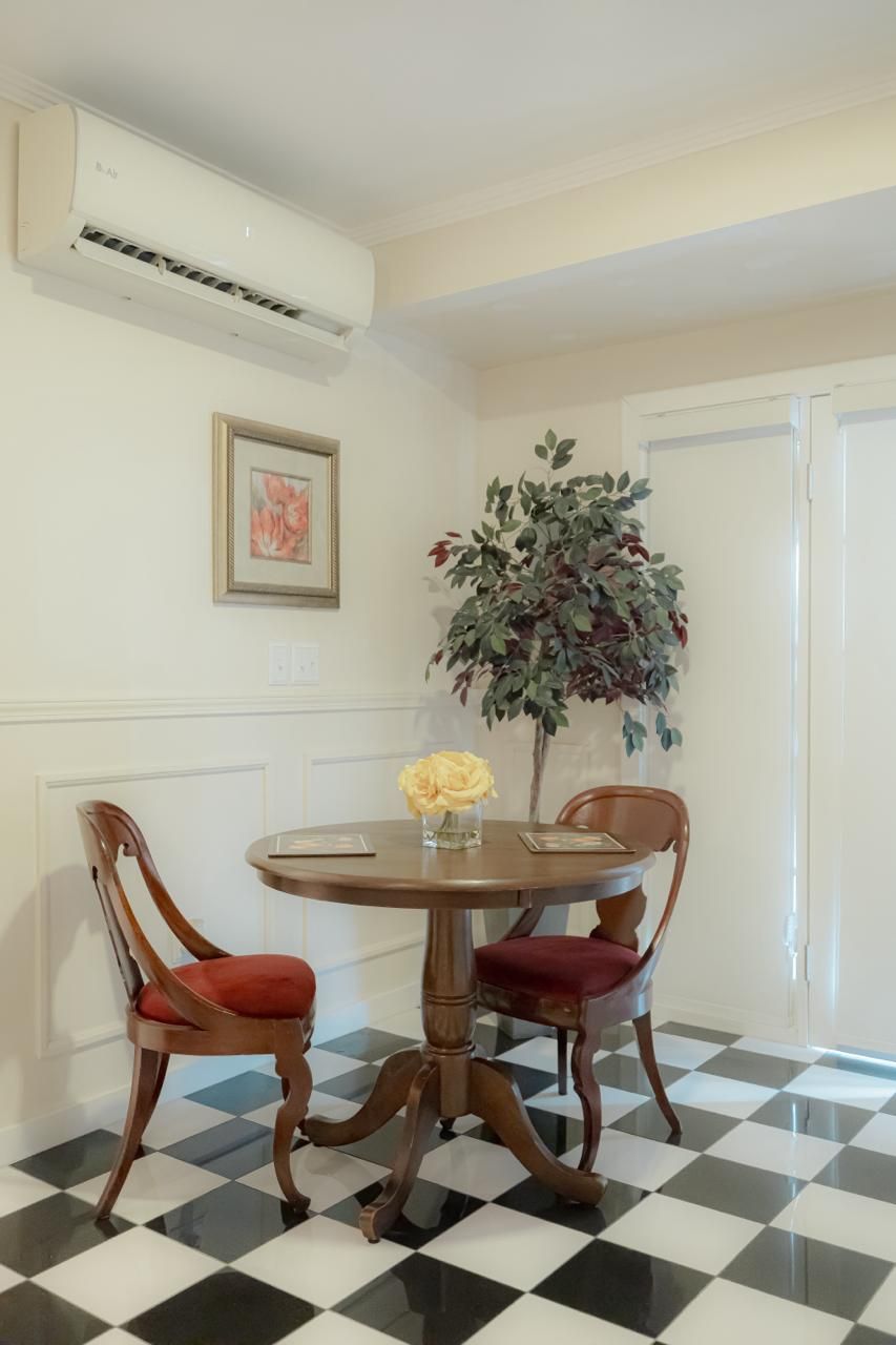 A dining area with a round table, two chairs, a potted plant, and a framed picture on the wall.