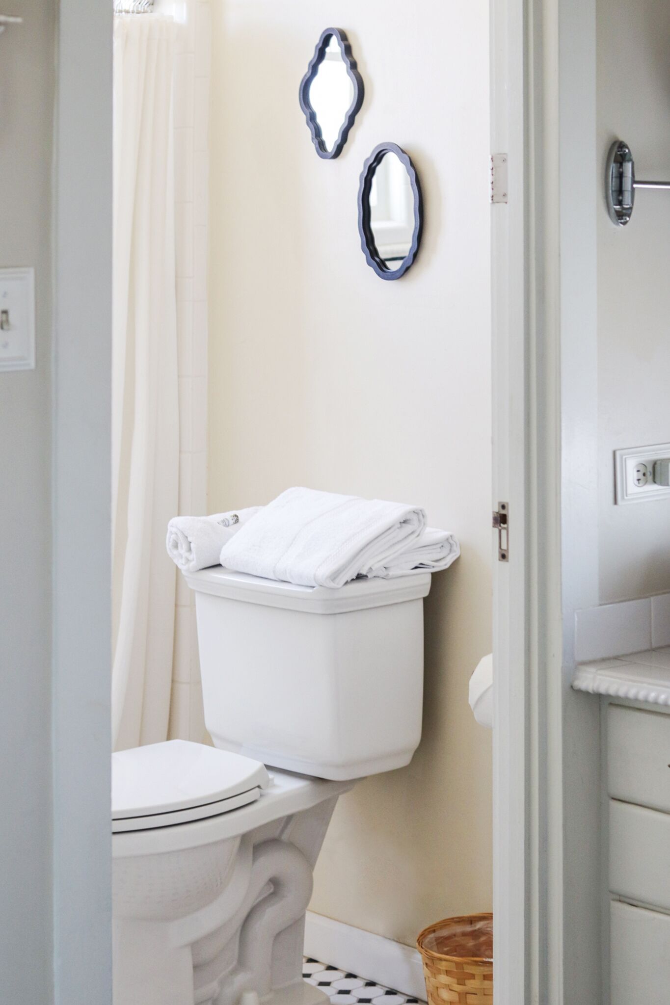 Des toilettes blanches avec un abattant et un couvercle blancs, un rideau de douche blanc et deux miroirs muraux.