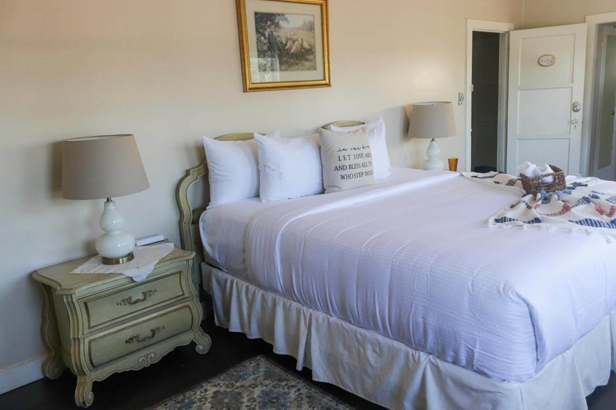 A neatly arranged bedroom with a bed, two bedside tables, a lamp, a framed picture on the wall, and a door.