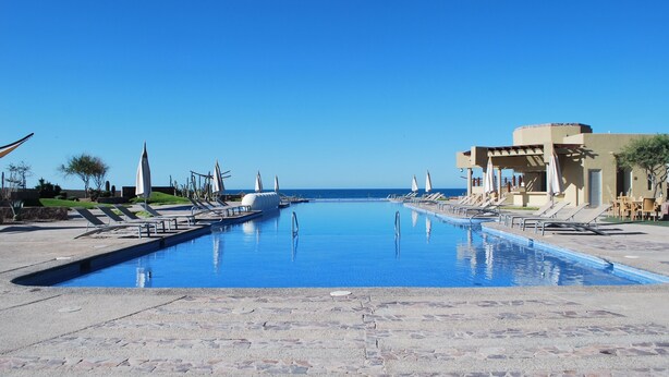 A swimming pool with lounge chairs and a building in the background. - Encanto Living 1201 -4BR by Kivoya (Puerto Peñasco)