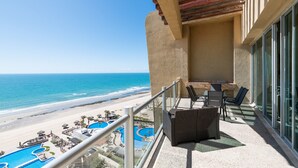 A balcony with a view of the beach and ocean, outdoor seating, and a pool area. - Encanto Living 1201 -4BR by Kivoya (Puerto Peñasco)