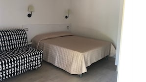 A small, simple room with a bed, a chair, and an air conditioning unit.