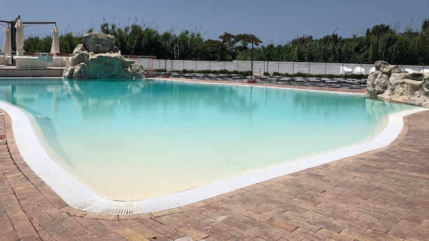 A swimming pool with a clear blue water, surrounded by a brick deck and a white safety border.