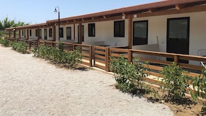 A row of single-story cabins with wooden railings, each featuring a door and windows, set against a clear sky.