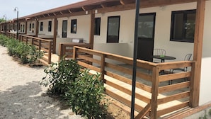 A row of wooden-framed cabins with outdoor seating areas, each featuring a door and windows.