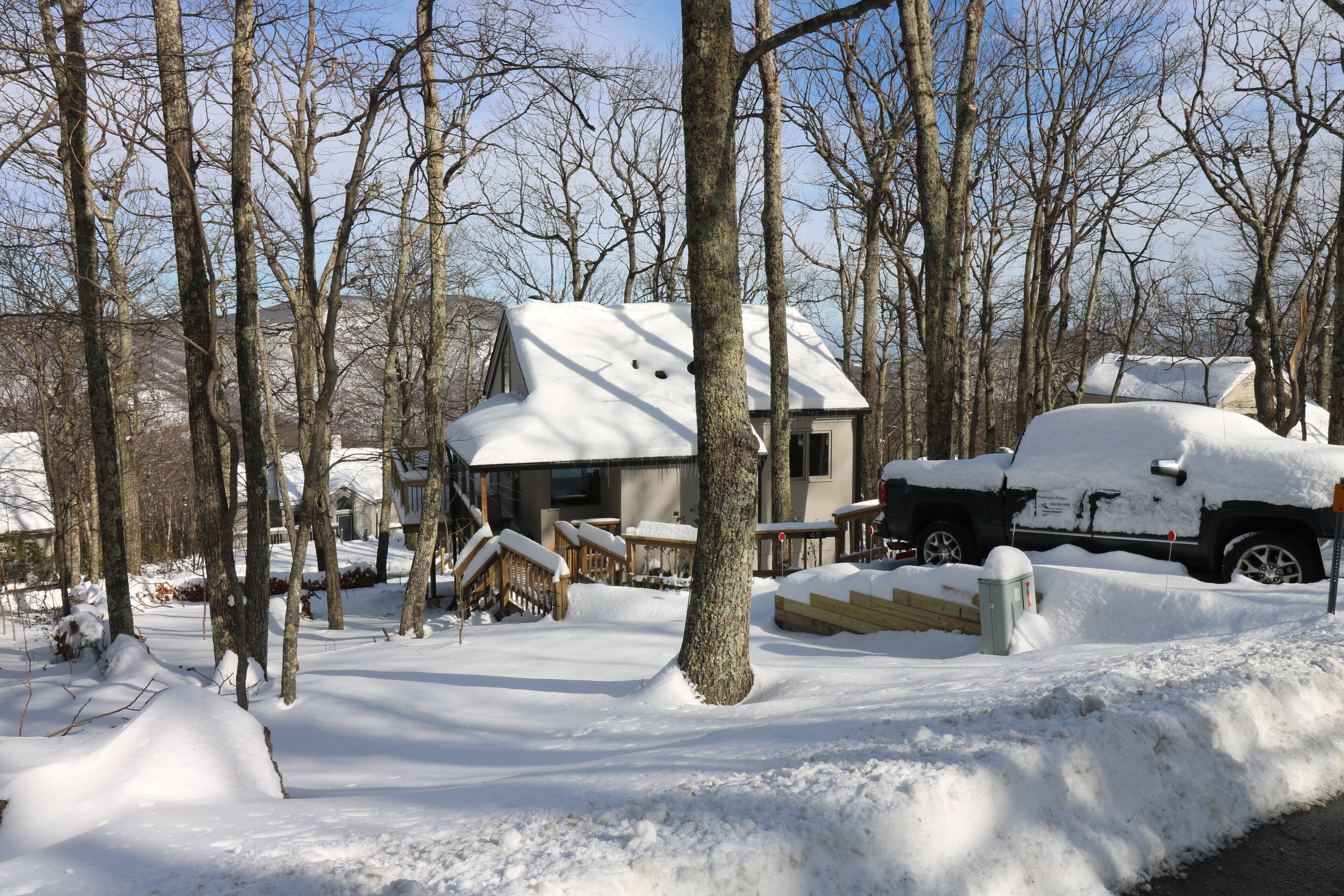 Un quartier résidentiel enneigé, avec une maison, un véhicule garé et une terrasse en bois.
