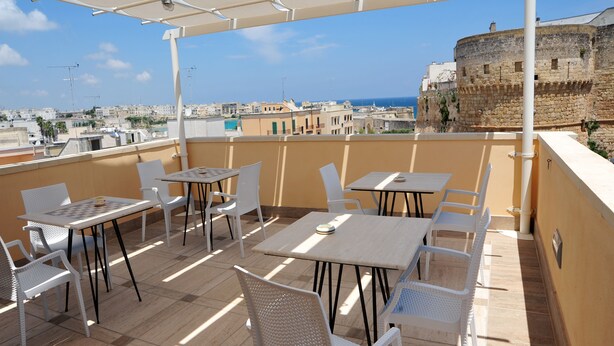 A rooftop terrace with outdoor seating, a view of the cityscape, and a historic building in the background. - Camere Sulle Mura (Otranto)