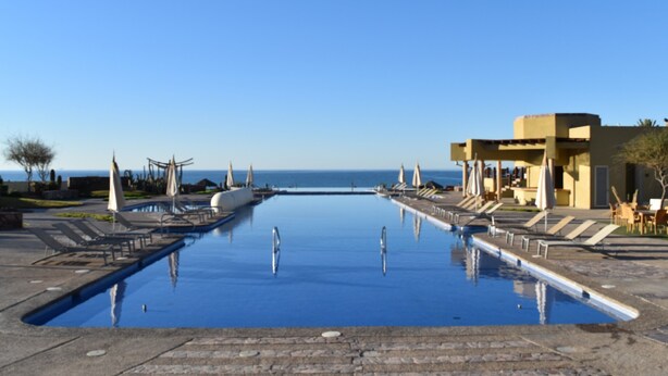 A swimming pool with lounge chairs and umbrellas, a building with a flat roof, and a clear view of the sea. - Encanto Living 1202 -4BR by Kivoya (Puerto Peñasco)