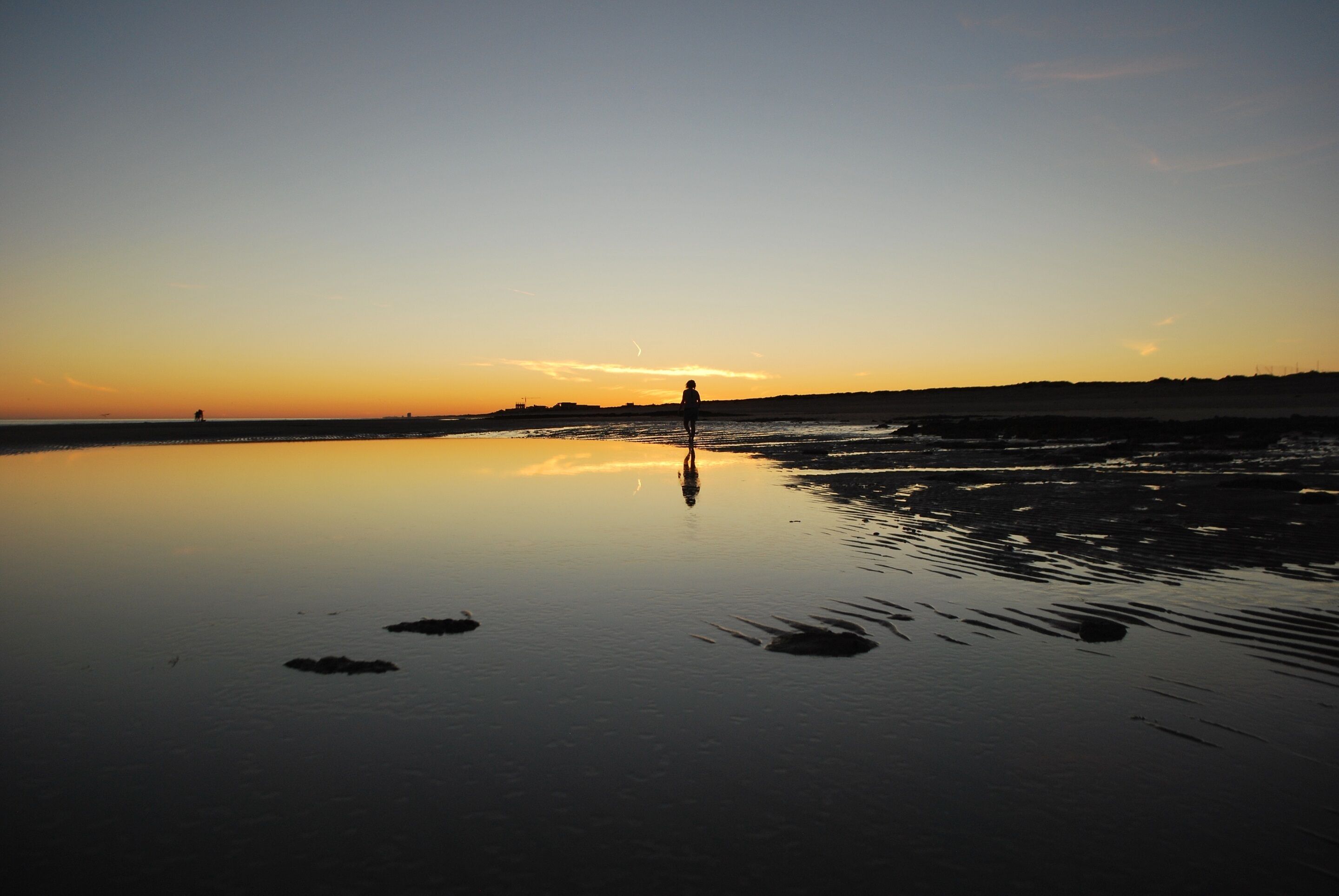 A beach at sunset with calm waters reflecting the sky.