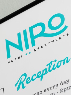 A hotel reception sign with the name "NIO HOTEL APARTMENTS" and the word "Reception" prominently displayed.