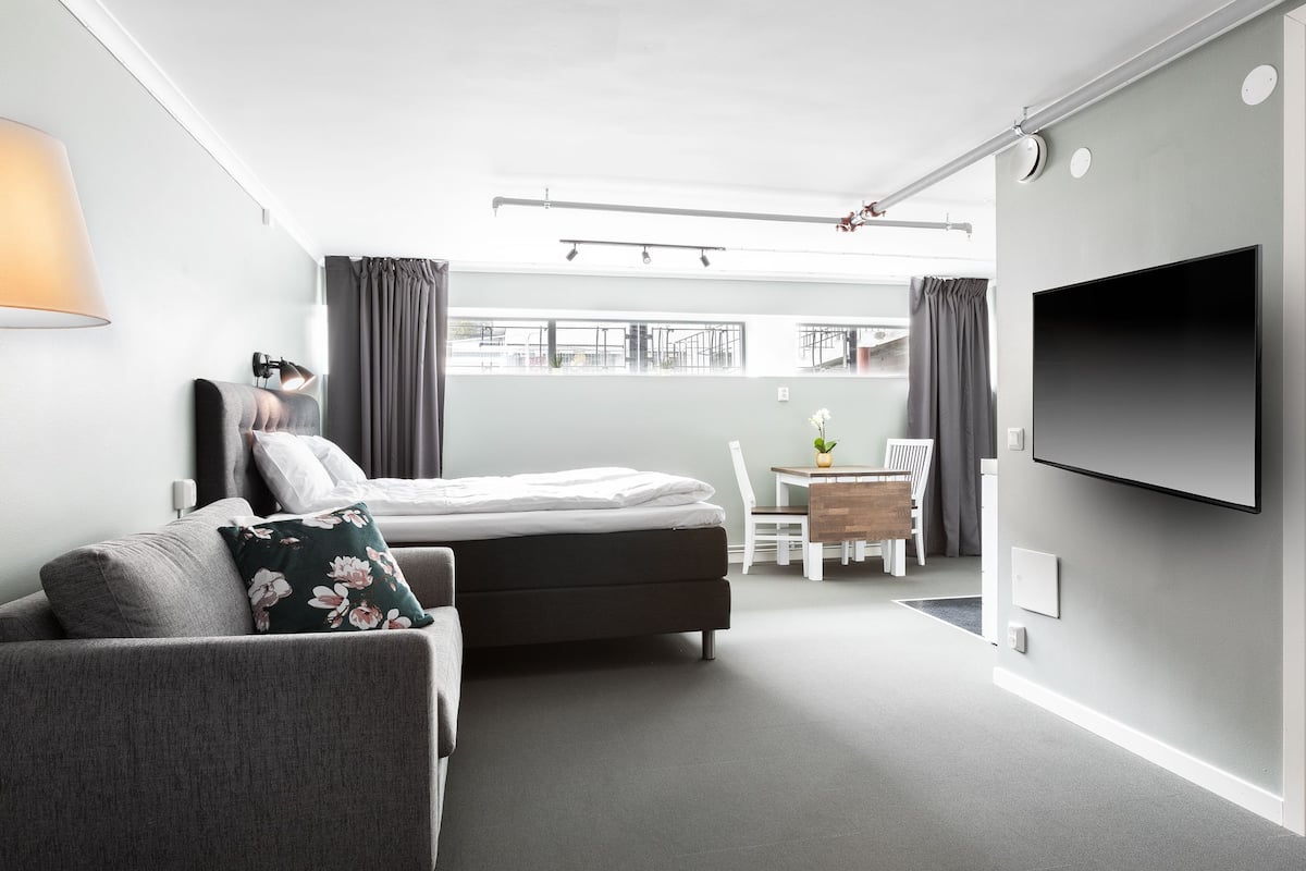 A modern hotel room with a bed, a sofa, a desk, and a TV.