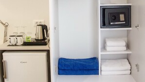 Habitación de hotel compacta con kitchenette, armario con ropa colgada, caja fuerte y un refrigerador pequeño.