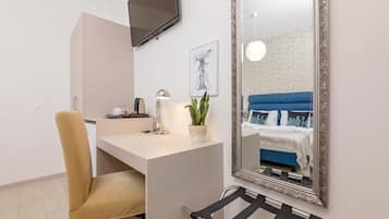 Una habitación moderna con escritorio, silla y un espejo grande que refleja una cama con ropa de cama azul.