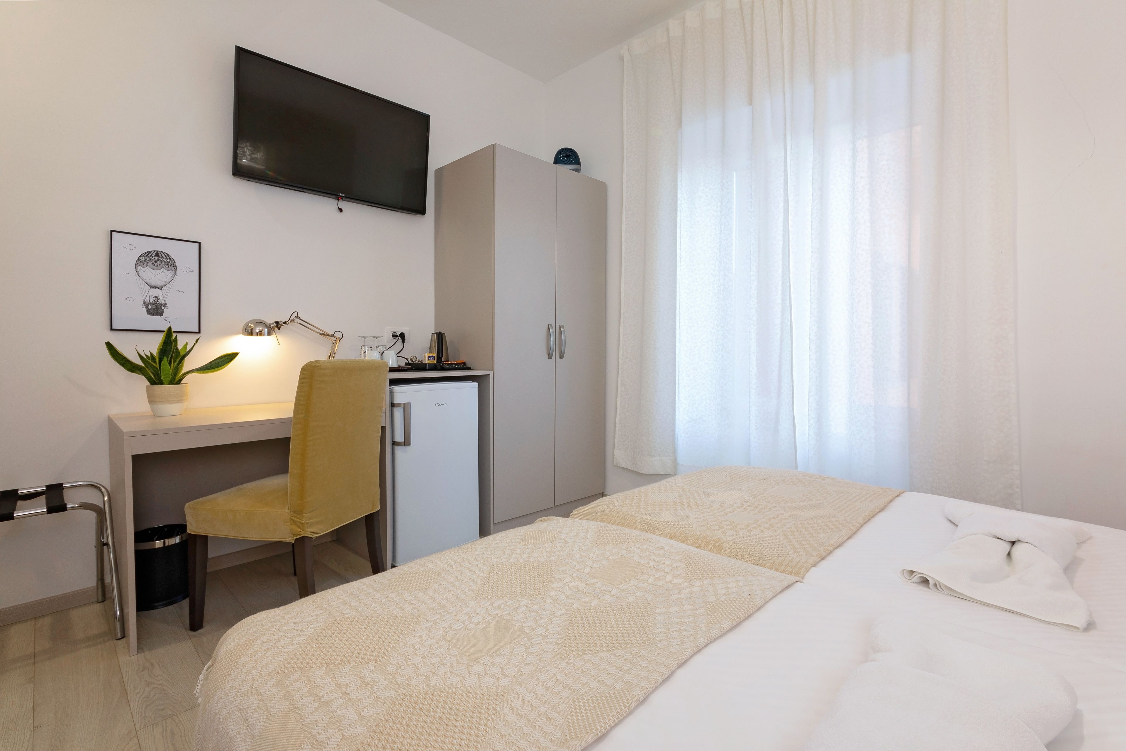 Ein Hotelzimmer mit Bett, Schreibtisch mit Stuhl, Fernseher, Kleiderschrank und einem Fenster mit Vorhängen.
