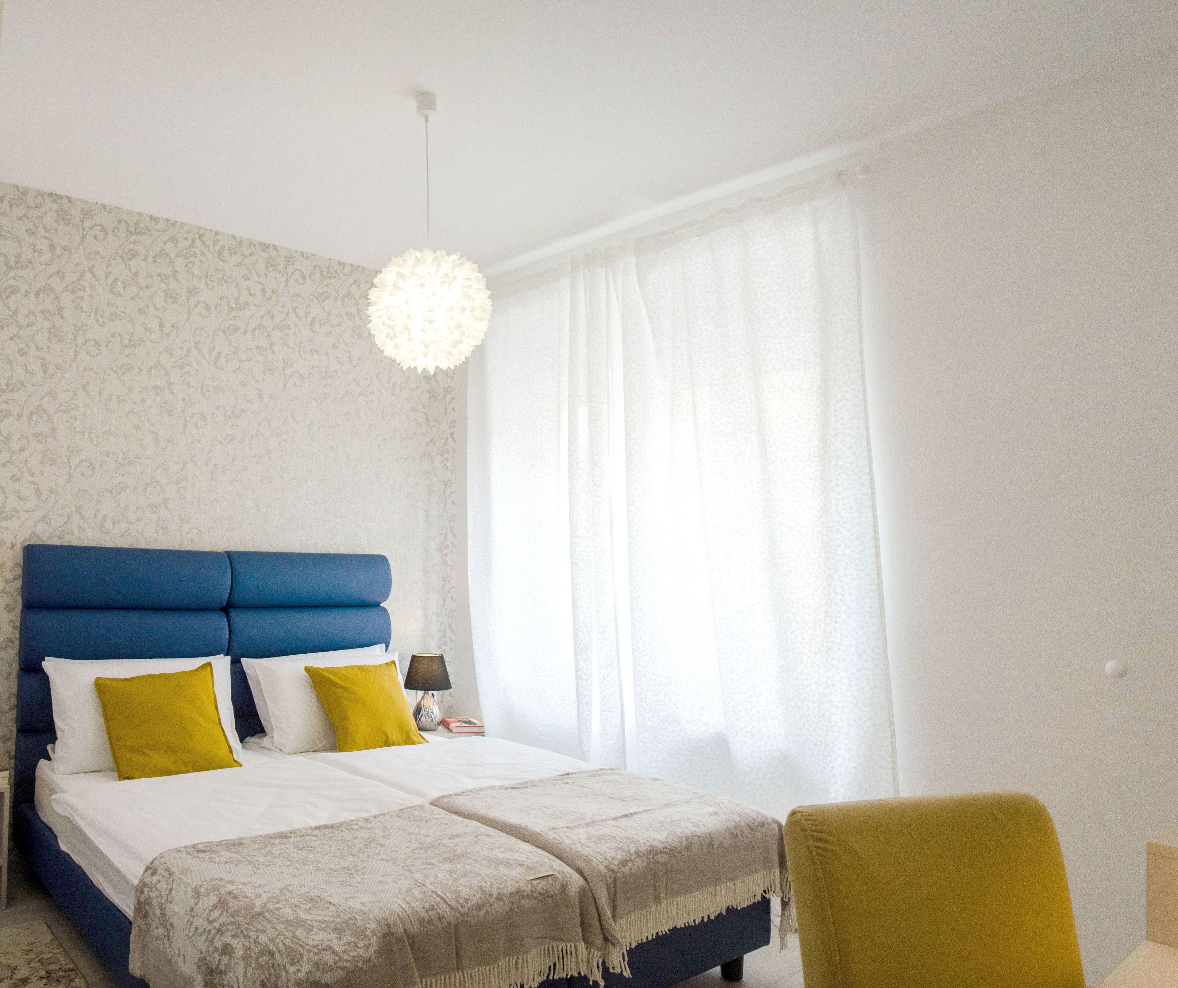 Un dormitorio con cabecera azul, ropa de cama blanca y una silla amarilla.