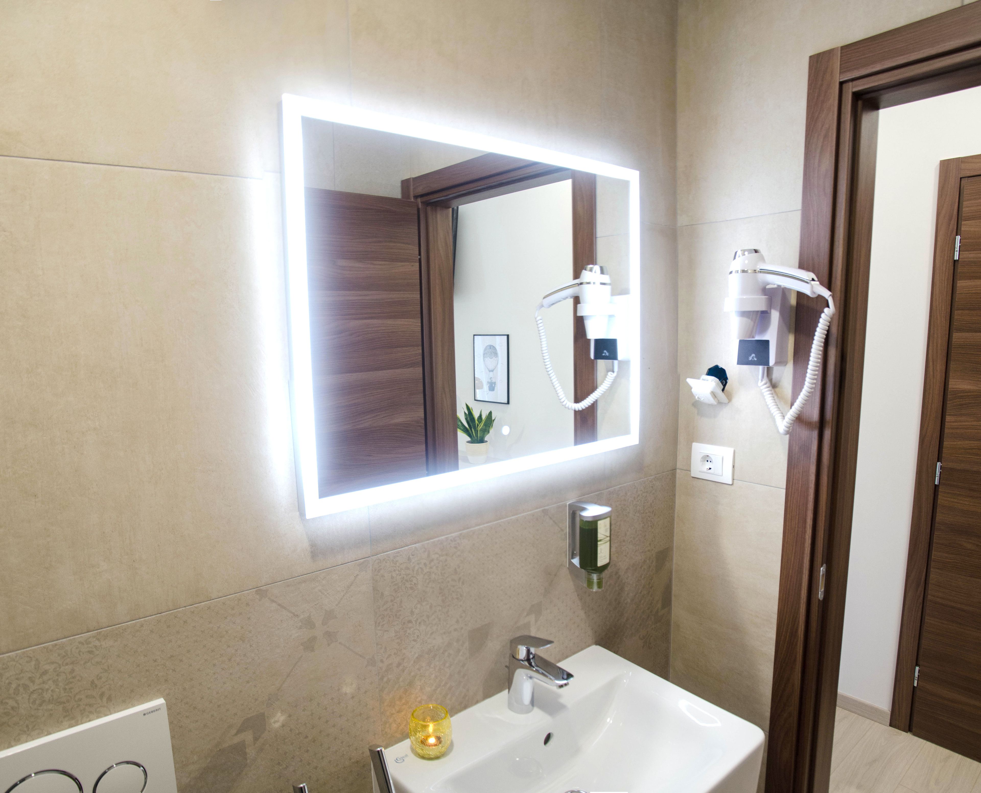 A bathroom with a large mirror, a sink, a handheld showerhead, and a wall-mounted hairdryer.
