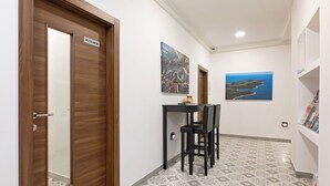 Un pasillo con una puerta de madera que indica “KITCHEN”, una mesita con sillas y dos cuadros colgados en la pared.