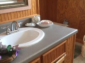 A bathroom with a white sink, wooden cabinets, and a mirror above the sink. - Music Garden Mansion (San Angelo)