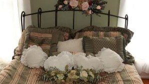 Una cama con estructura metálica, varias almohadas y un arreglo floral sobre el edredón.