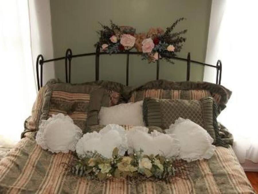 A bed with a metal frame, multiple pillows, and a floral arrangement on the bedspread.