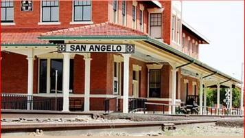 Una estación de tren con un letrero destacado que dice 'SAN ANGELO', un área de espera cubierta y fachada de ladrillo.