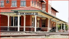 A train station with a prominent 'SAN ANGELO' sign, covered waiting area, and a brick building facade. - Music Garden Mansion (San Angelo)