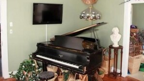 Una habitación con un piano de cola, un televisor montado en la pared y un techo decorativo.