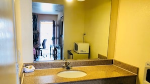 A bathroom with a granite countertop, a sink, a mirror, and a microwave. - Bayshore Inn (San Jose)