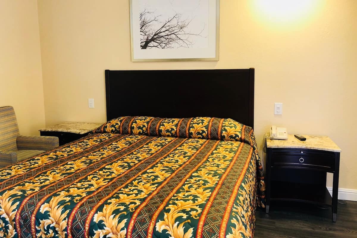 A hotel room with a bed, a nightstand, a chair, and a framed picture on the wall.